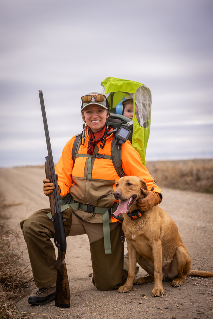 A hunter with baby carrier and yellow lab on a prairie road