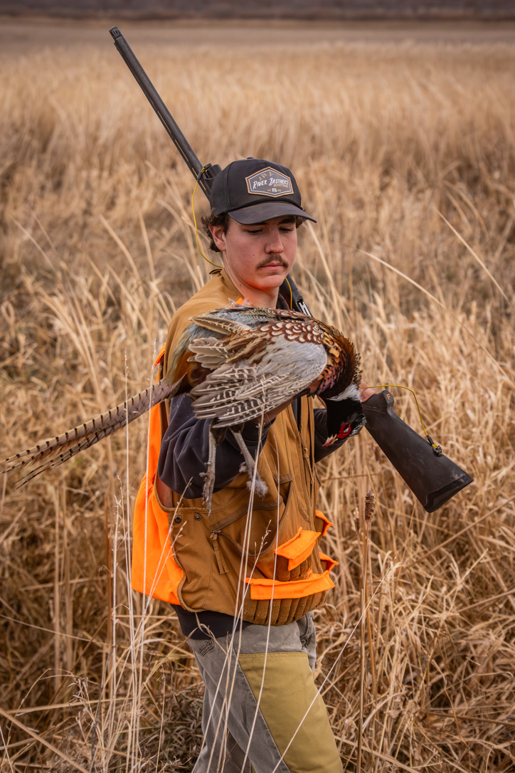 Young hunter holding a rooster in the prairie grass