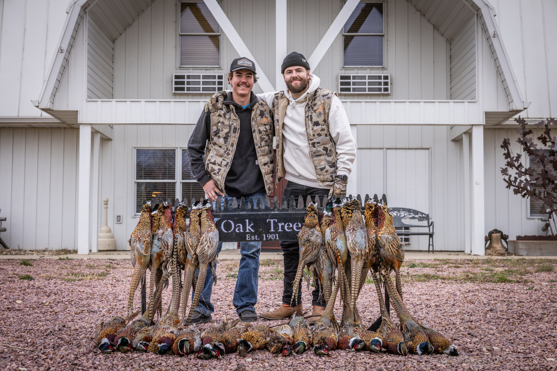 Two hunters posing behind the Oak Tree sign with the morning's birds
