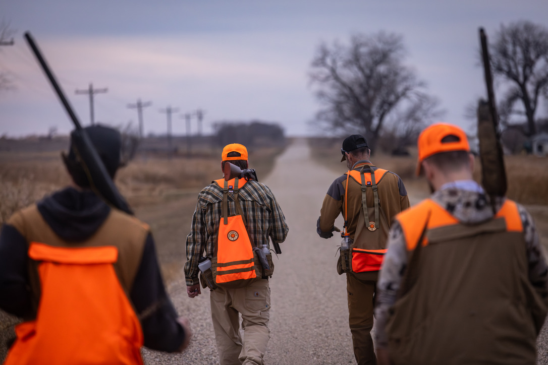 Four hunters walking down a gravel road at dawn