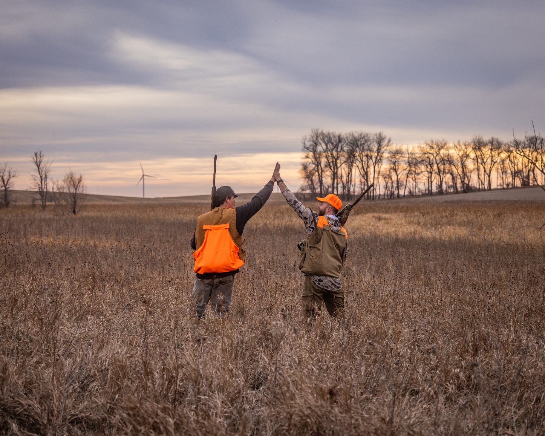 Two hunters high-fiving in the prairie at sunset